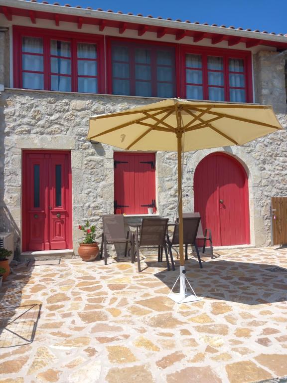 a table with an umbrella in front of a building with red doors at Sweet Red Home in Asprogerakata