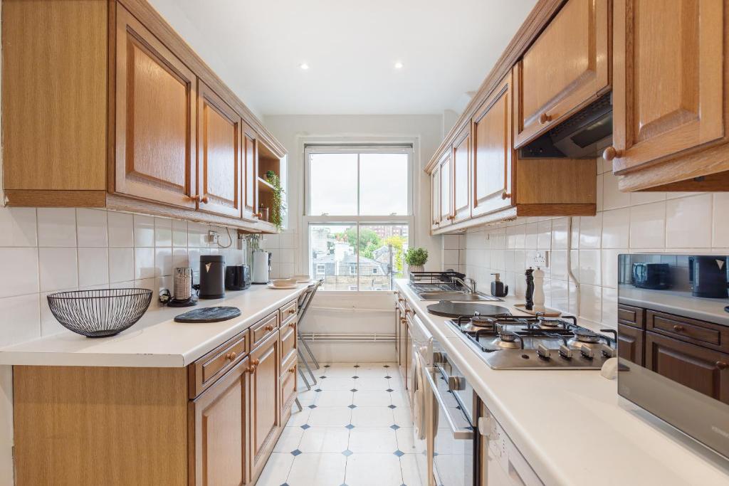 Queens Gate Bliss 1 في لندن: مطبخ كبير مع دواليب خشبية ونافذة