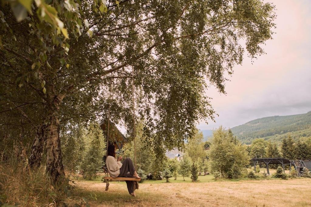 a woman sitting on a swing under a tree at Polna Mięta in Stronie Śląskie
