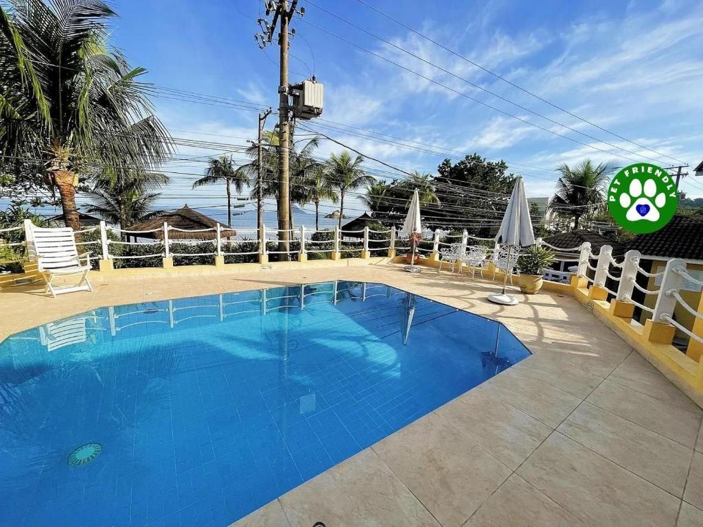a large blue swimming pool with a fence and the ocean at Home 80 I Casa em condomínio pé na areia em Juquehy WIFI e Piscina in São Sebastião
