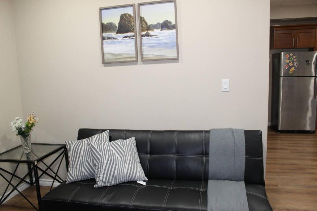 Un canapé en cuir noir dans un salon avec deux tableaux au mur dans l'établissement Tranquille pond facing suite, à Nisku