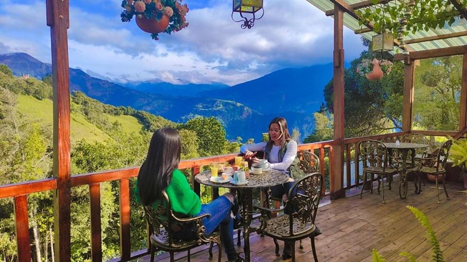 dos mujeres sentadas en una mesa en una terraza con vistas en Las Orquídeas Runtun, en Baños