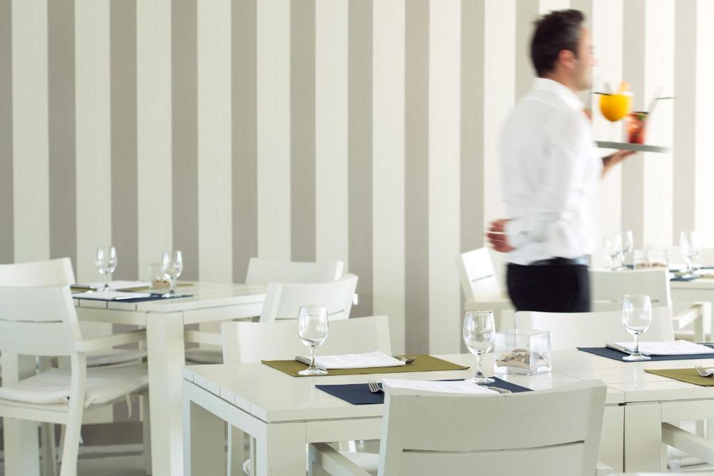 a man standing in a dining room with white tables and chairs at Troia Design Hotel in Troia