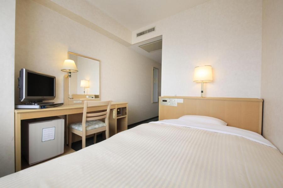 甲府市にある甲府 ワシントン ホテル プラザのベッド、デスク、テレビが備わるホテルルームです。