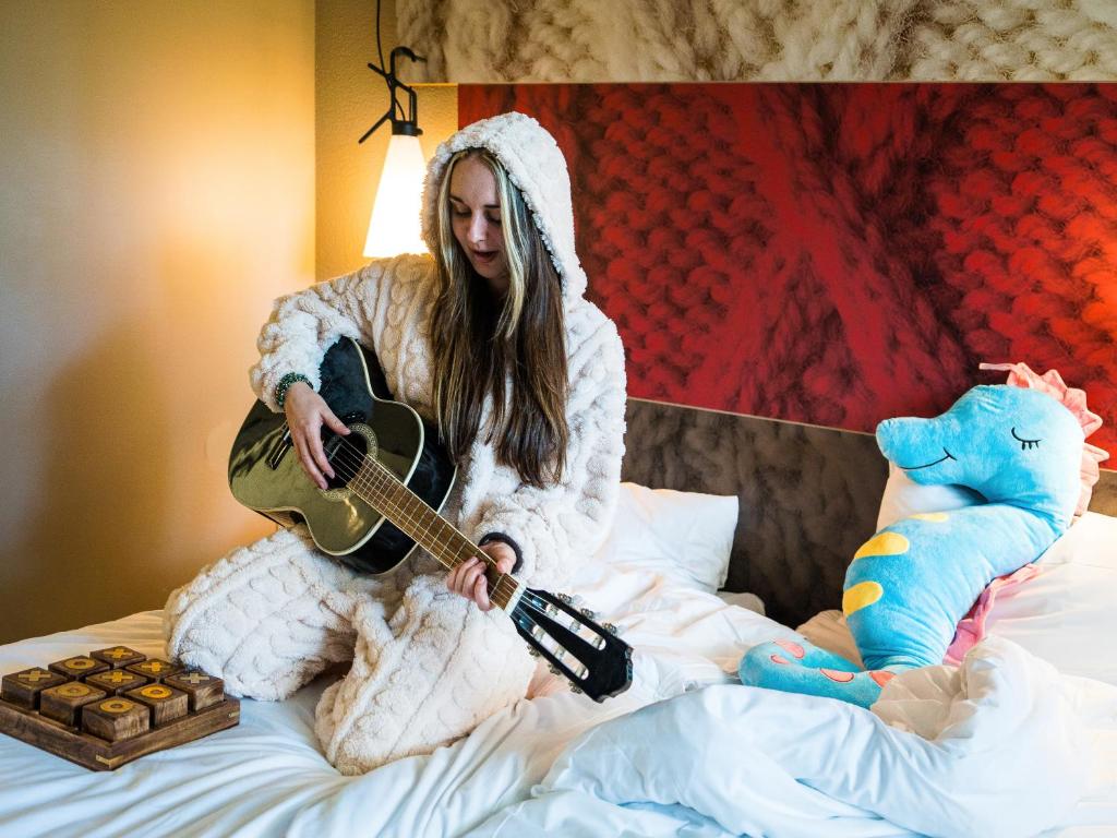 Eine Frau, die auf einem Bett sitzt und Gitarre spielt. in der Unterkunft ibis Arcachon la Teste de Buch in La Teste-de-Buch