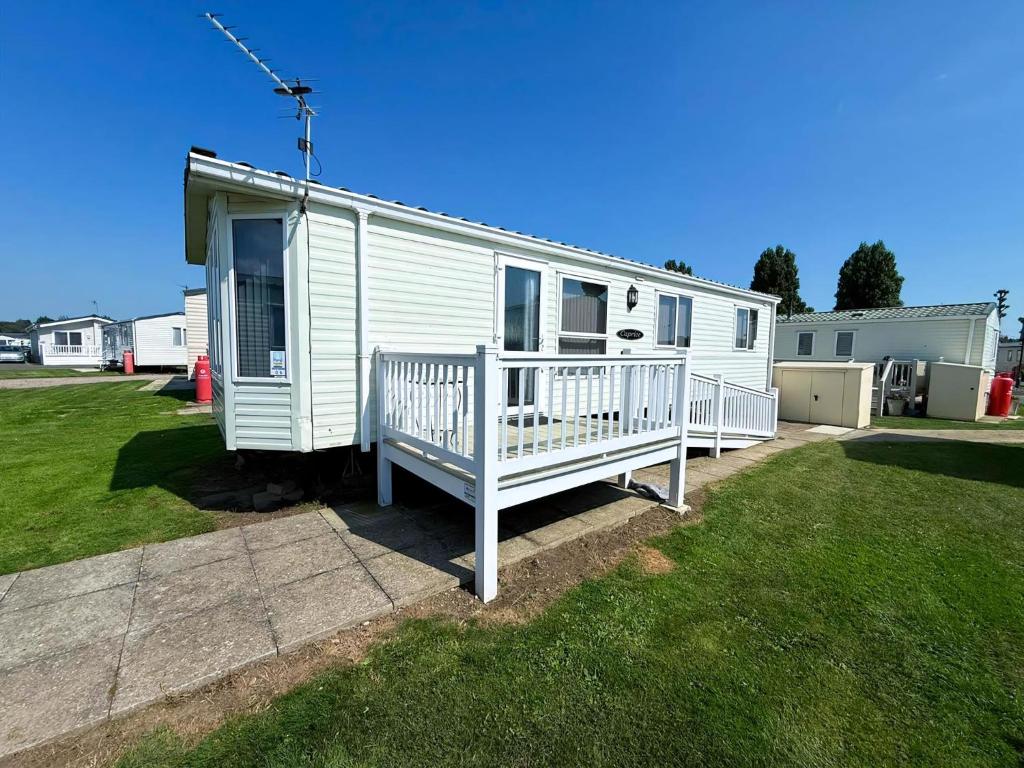 a white mobile home with a porch and a yard at Lovely Caravan With Wifi & Decking At Felixstowe Beach Holiday Park Ref 55005Sw in Walton