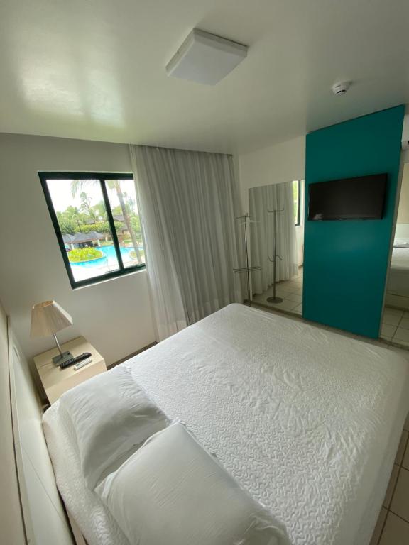 ein Schlafzimmer mit einem weißen Bett und einem Fenster in der Unterkunft Marulhos Resort by HomeTemp in Porto De Galinhas