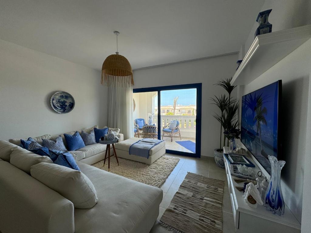 ein Wohnzimmer mit einem weißen Sofa und einem Fernseher in der Unterkunft A Luxurious & Cozy Apartment Greek Village Marassi in El-Alamein