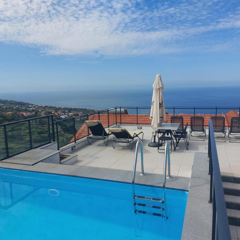 ein Swimmingpool mit Stühlen, Tisch und Sonnenschirm in der Unterkunft Paradise Point Sea & Mountain view in Estreito da Calheta