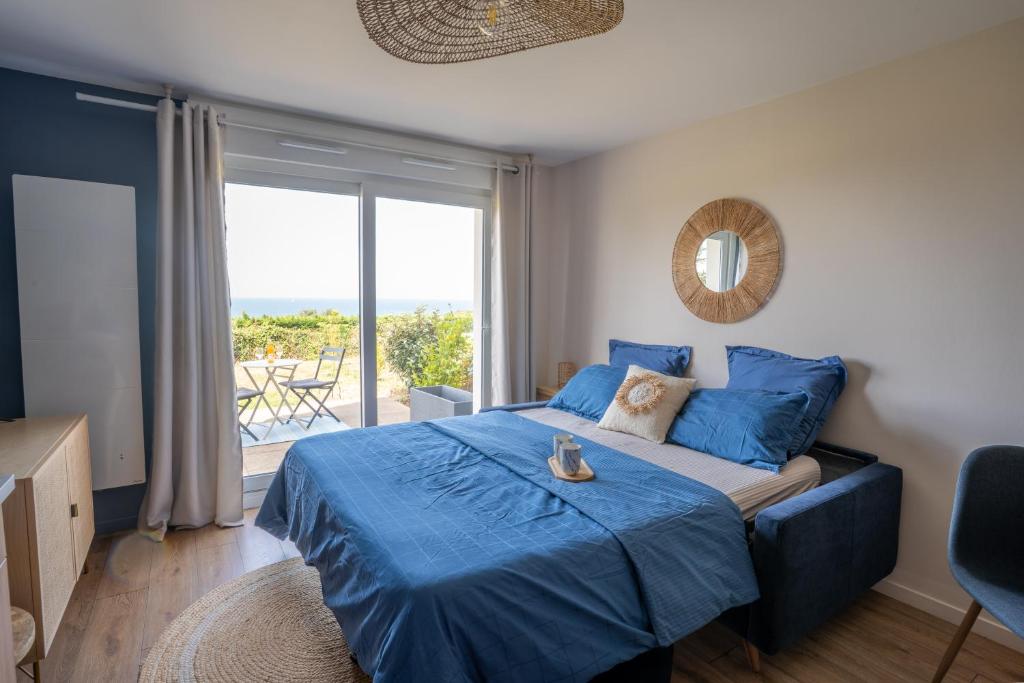 a bedroom with a blue bed and a large window at Bienvenue au studio L'escale Bleue avec vue mer et sur le Cap Frehel in Saint-Cast-le-Guildo