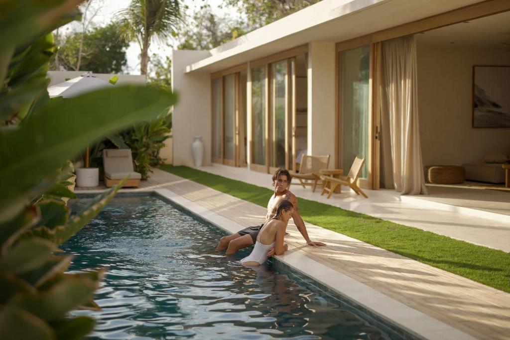 a man and a woman sitting in a swimming pool at COZ Bali Boutique Villas walking distance to Padang Padang Beach in Uluwatu