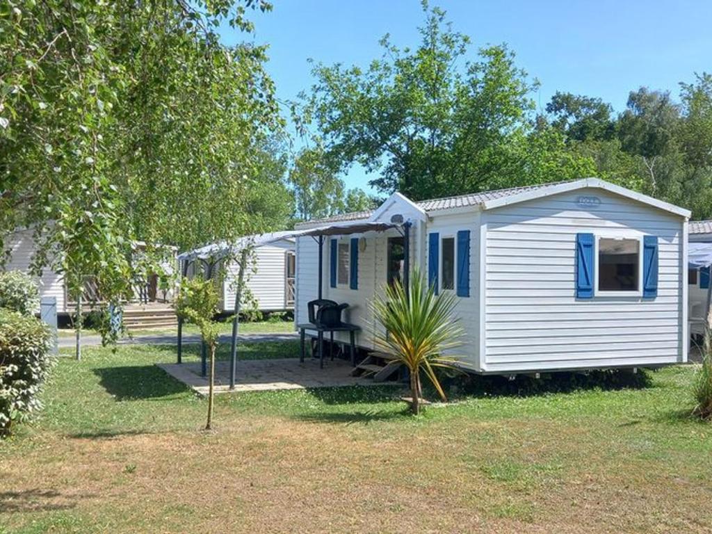 a small white caravan with blue shutters on a yard at Mobil Home Confortable avec Terrasse - API-1-52-390 in Saint-Sornin