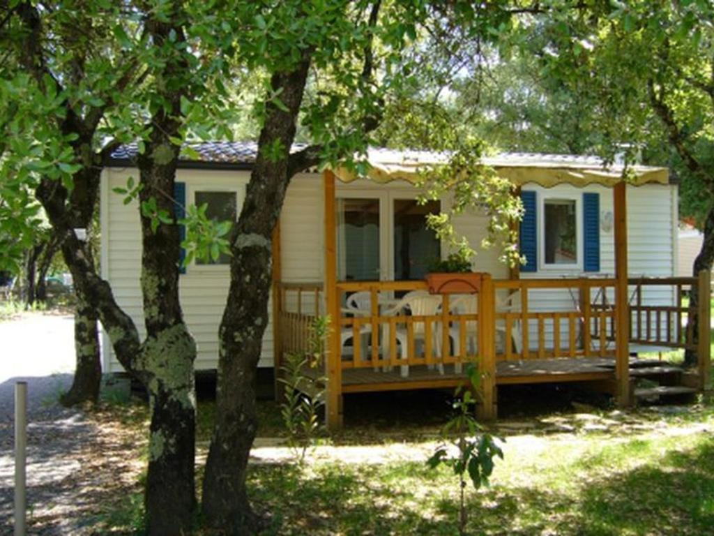a small white house with a large wooden porch at Mobil home 6 pers avec terrasse - API-1-52-222 in Saint-Maurice-dʼIbie