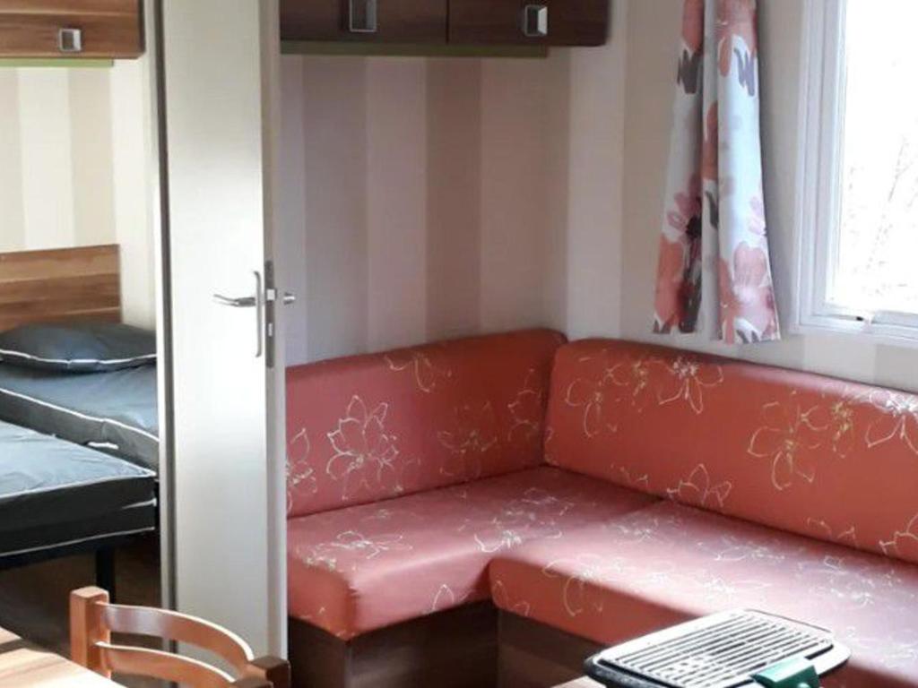 a red couch sitting in a room with a table at Mobil-Home Confortable 3 Chambres avec Terrasse - API-1-52-399 in Saint-Sornin