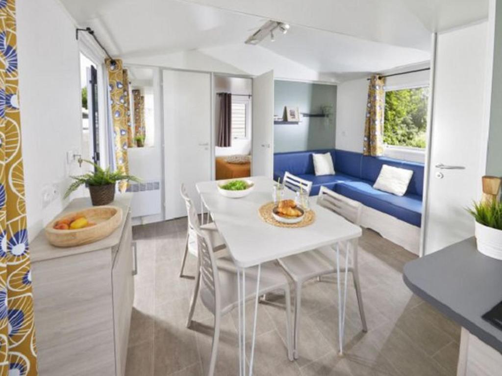 a kitchen and living room with a white table and a blue couch at Mobil-home avec Terrasse pour 6 Personnes en Ardèche - API-1-52-360 in Saint-Maurice-dʼIbie