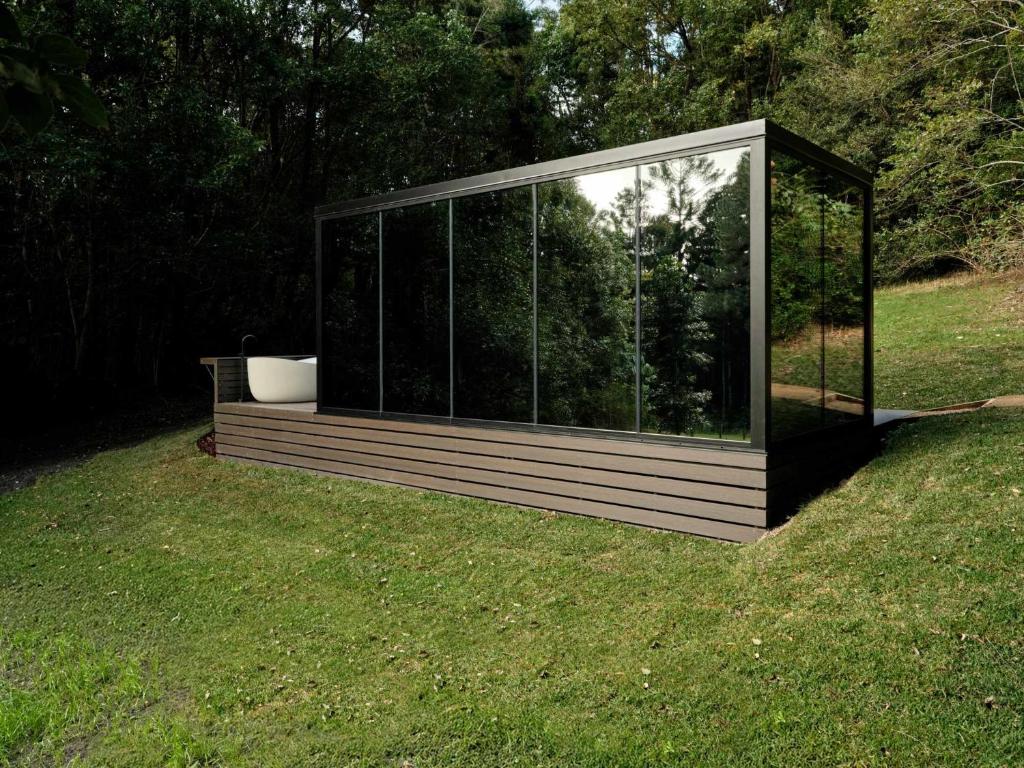 a glass house with a tub in the grass at Luxury Mirror Home In Byron Bay in Byron Bay