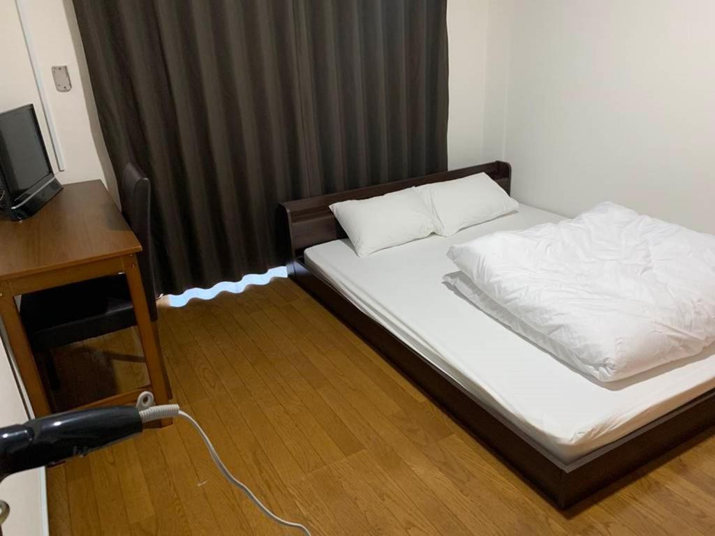 a bedroom with a bed with white sheets and a television at AO Dazaifu / Vacation STAY 61719 in Chikushino