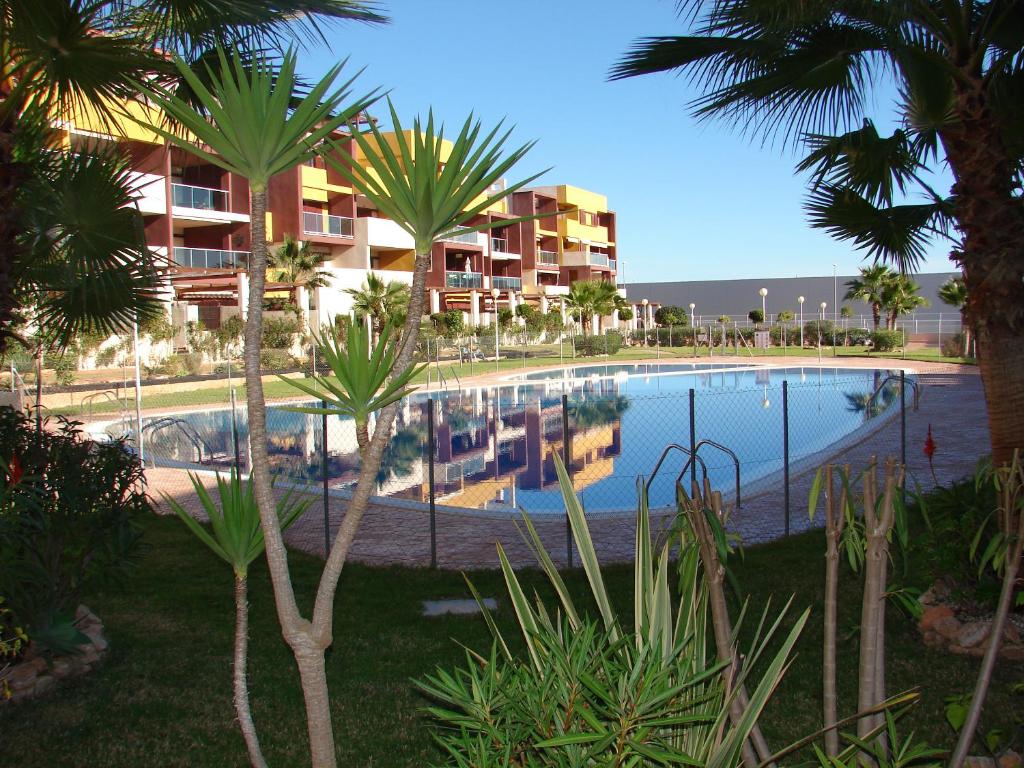 a swimming pool with palm trees in front of a building at Apartamento en Playa Flamenca (residencial El Bosque) in Playas de Orihuela