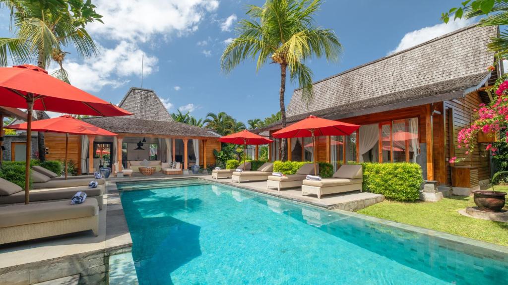 a pool with chairs and umbrellas next to a house at Villa Taramille by Villa Finder in Kerobokan