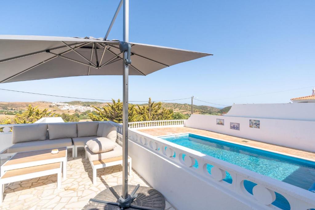 a villa with a swimming pool and an umbrella at Casa Dos Amigos in Budens