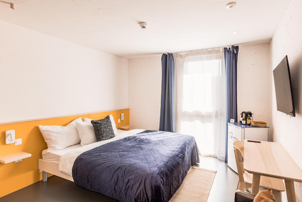 a bedroom with a bed and a desk and a window at N's Hotel - Self-Check-in Hotel in Kerzers