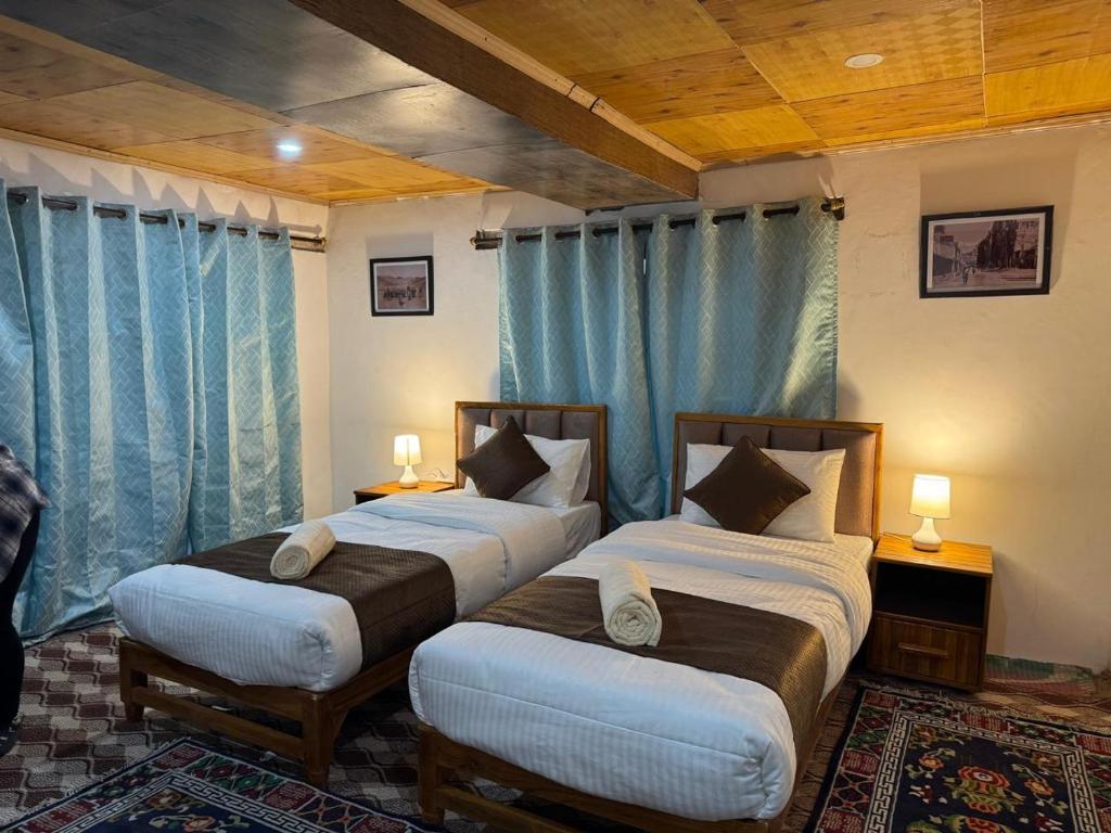 two beds in a room with blue curtains at Kurambik Eco Homestay in Dumkhar