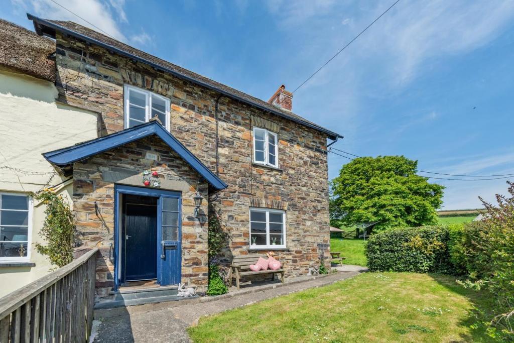 Una casa de piedra con una puerta azul y una persona sentada en un banco. en Buckinghams Leary, en West Buckland