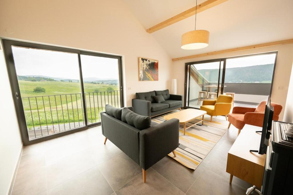 a living room with a couch and chairs and a balcony at Le 240, entre lac et montagnes in Les Rousses