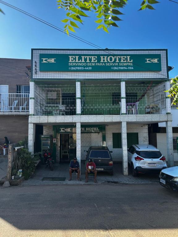 Dos hombres sentados frente a un hotel azul. en Elite Hotel 02, en Teresina