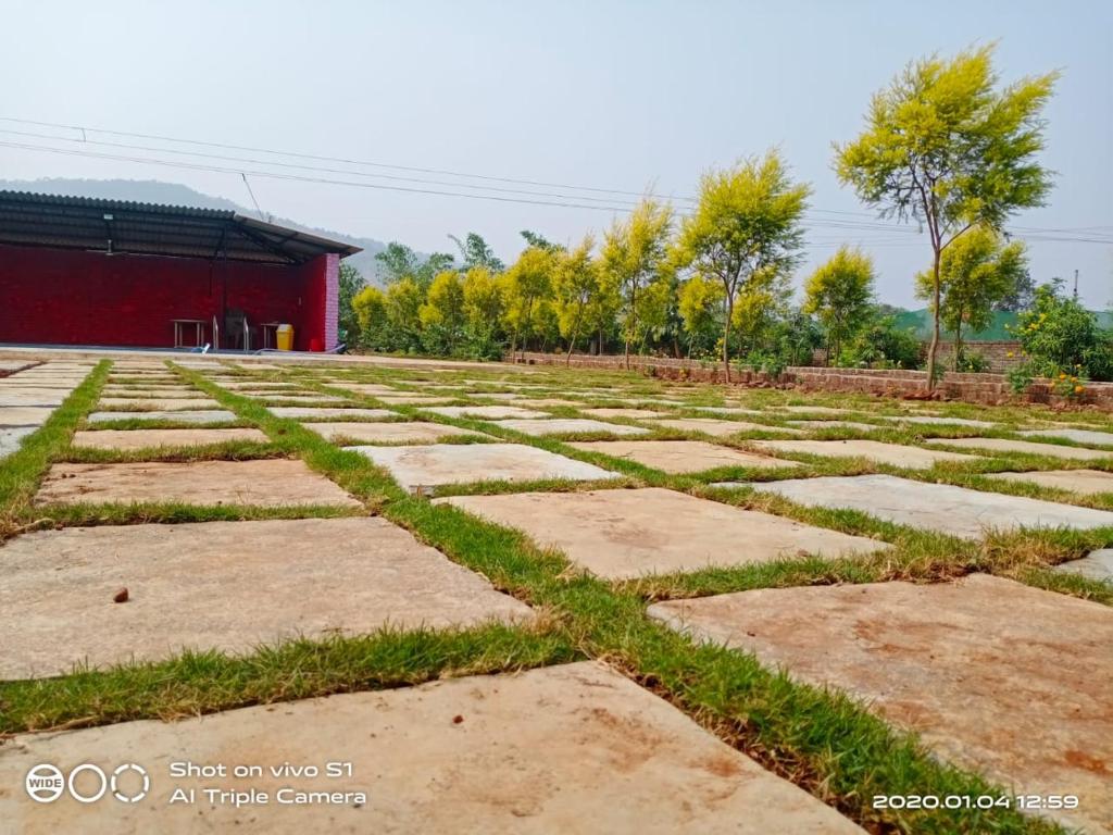 ein Feld mit Gras und Steinen vor einem roten Gebäude in der Unterkunft Bs patil farmhouse by Prashant Patil in Karjat
