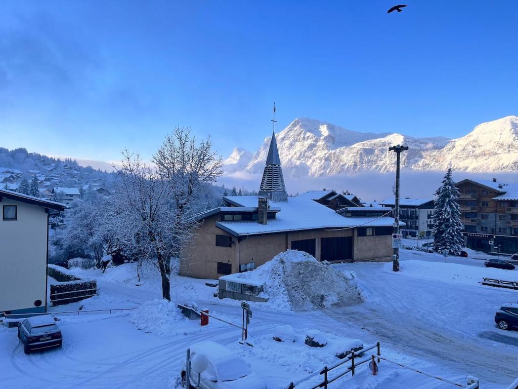 Un pueblo cubierto de nieve con una iglesia con campanario. en Joli studio hypercentre, en Les Carroz d'Araches