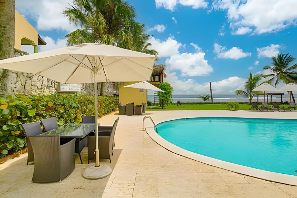 a patio with an umbrella and a table and chairs next to a pool at Caribbean Idyllic Vacation at Beachfront 1-BR Apt. in Juan Dolio