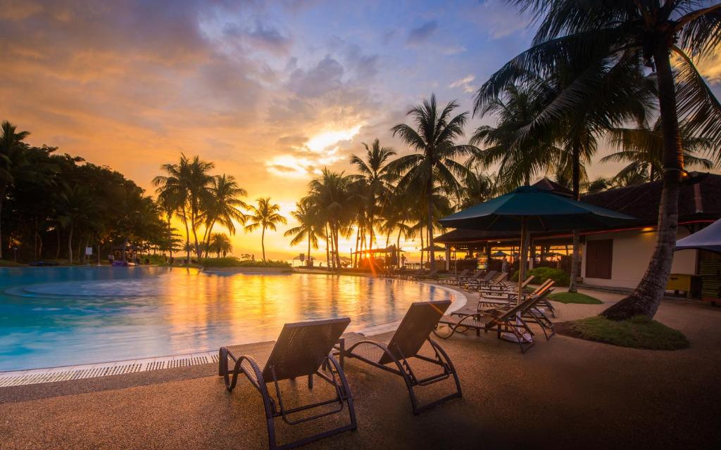 a resort pool with chairs and palm trees at sunset at The Pacific Sutera Hotel in Kota Kinabalu