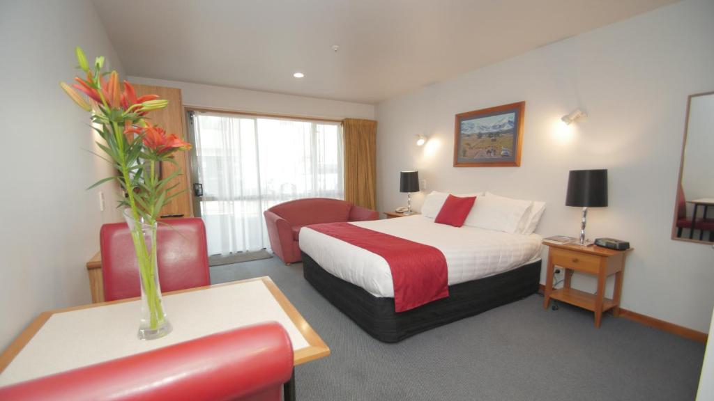 una habitación de hotel con una cama y un jarrón de flores en ASURE Christchurch Classic Motel & Apartments, en Christchurch