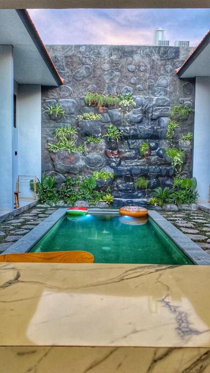 a swimming pool in front of a stone wall at Tropical Boho Loft Villa with Sofa Beds in Canggu