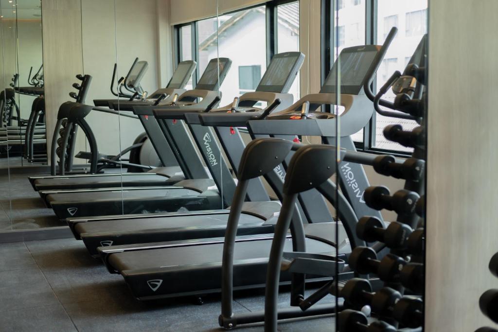 A bright gym with a row of treadmills, elliptical machines and a dumbbell rack.