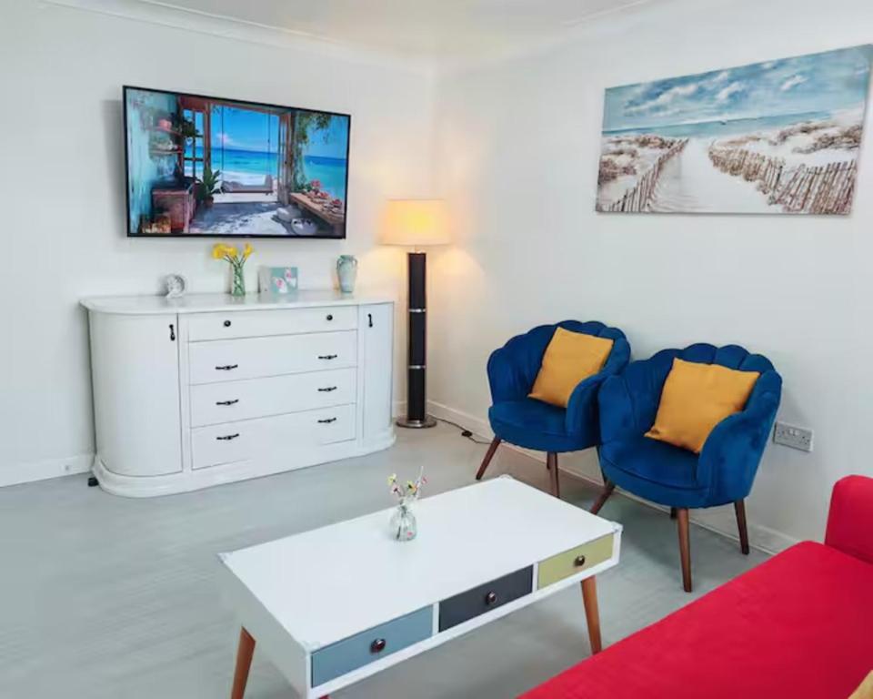 a living room with two blue chairs and a white dresser at Fully accessible bungalow by the Beach in Port Talbot