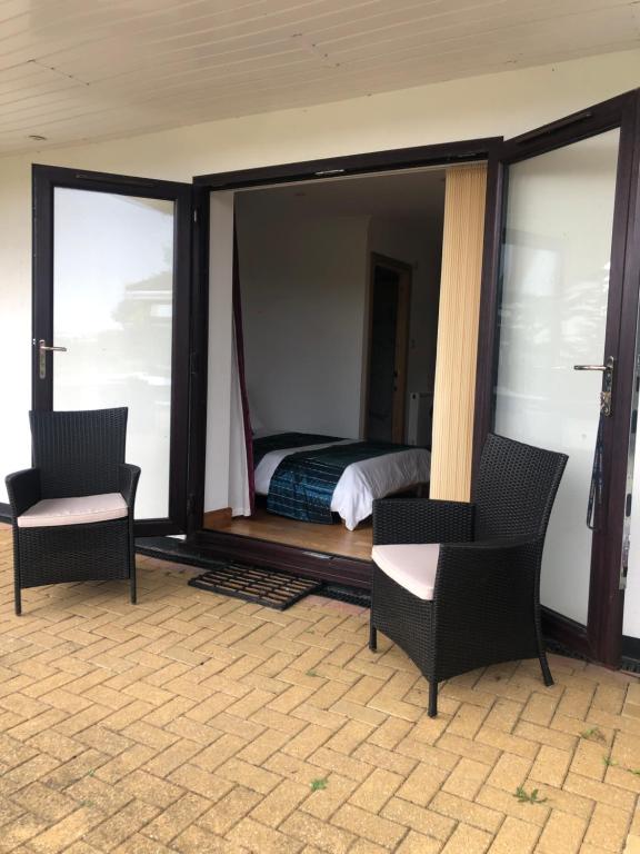 a bedroom with a bed and two chairs and windows at Gannel View Apartment in Newquay