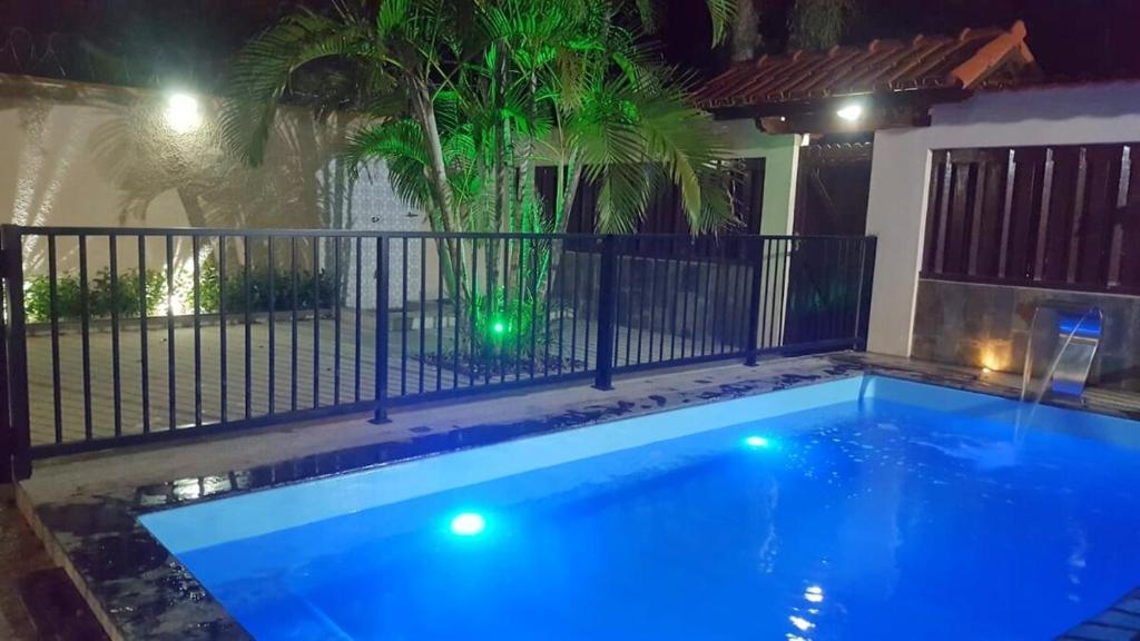 a swimming pool at night with a fence and a palm tree at Casa Duplex com piscina Praia de Santa Monica - Guarapari ES in Guarapari