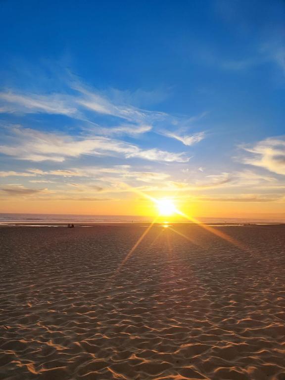 a sunset on a beach with the sun in the sky at Caparica Beach Stay in Costa da Caparica