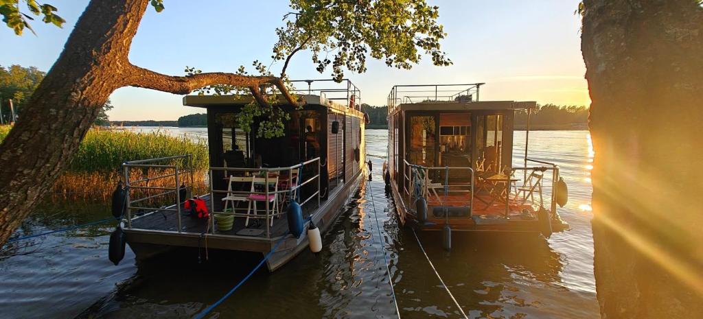 two boats are docked on the water near a tree at Domki pływające HouseBoat4U in Ruciane-Nida