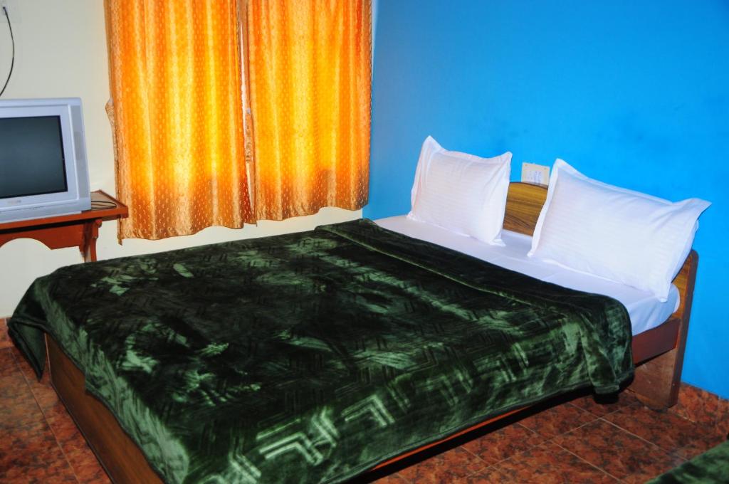 een bed met witte kussens en een televisie in een kamer bij Hotel Zaraa in Ooty