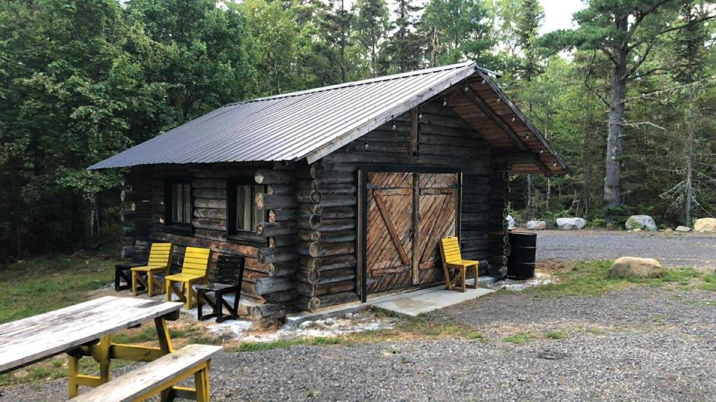 a small log cabin with yellow chairs and a picnic table at Le Shed - 2 personnes in Saint-Siméon