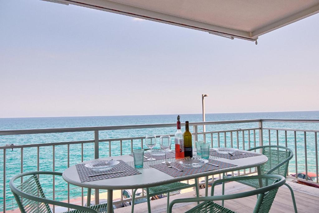 a table with wine bottles and chairs on a balcony overlooking the ocean at Amazing Oceanfront 2br in Oropesa del Mar