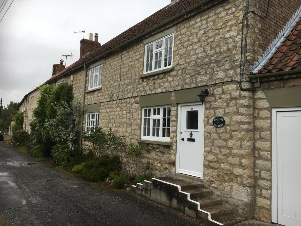 a stone house with a white door and stairs at Willow Cottage in Settrington