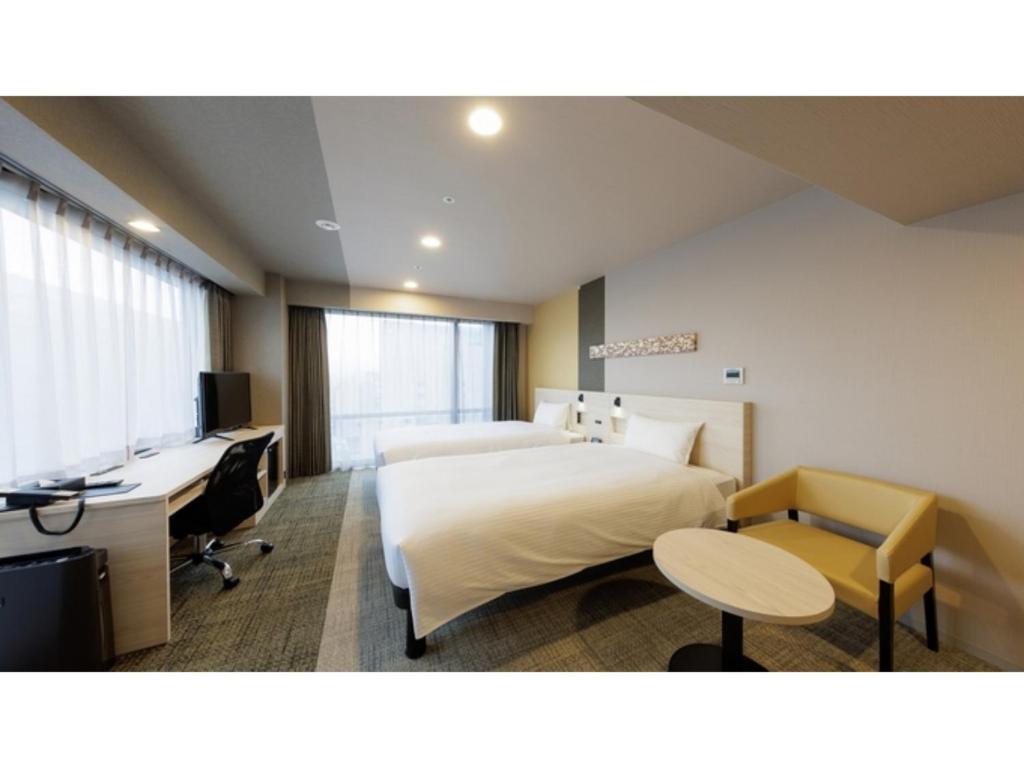ein Hotelzimmer mit zwei Betten und einem Schreibtisch in der Unterkunft Smile Hotel Kanazawa Nishiguchi Ekimae - Vacation STAY 11484v in Kanazawa