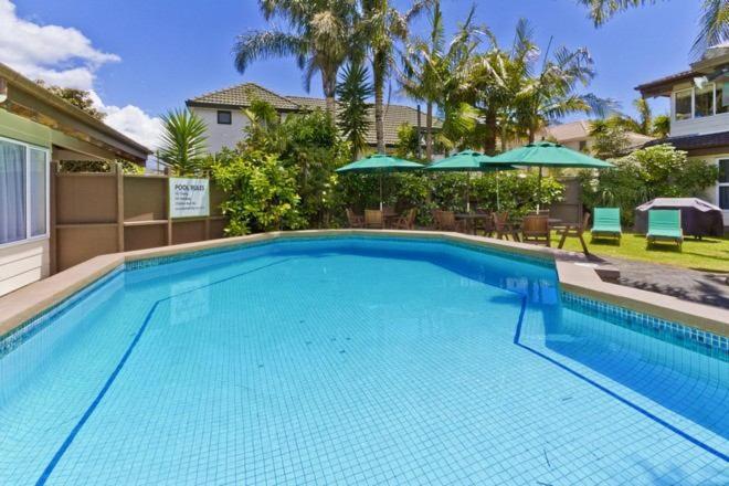 a large blue swimming pool with umbrellas at Takapuna Motor Lodge in Auckland