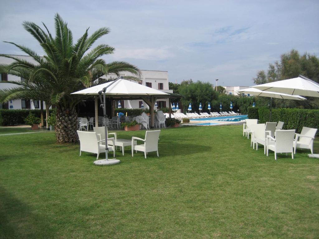 a row of white chairs and umbrellas on a lawn at Residence Club Barbara in Ostuni