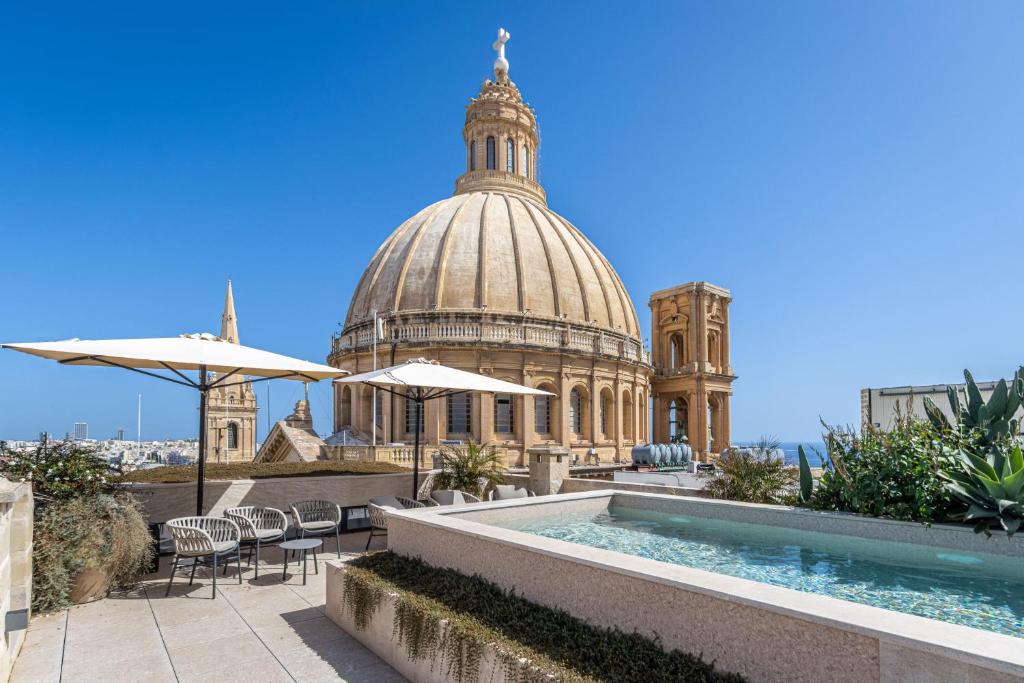 a building with a dome and a pool with chairs and umbrellas at Old Theatre Suites - Panarea in Valletta