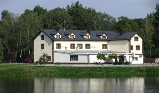 duży biały dom obok zbiornika wodnego w obiekcie Hotel Czardasz we Wrześni